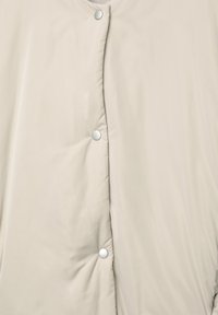 Gros plan d'un tissu beige matelassé avec trois boutons-pression argentés visibles le long de la couture centrale.