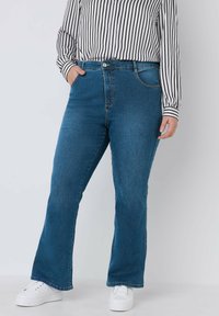 Jeans de mezclilla azul acampanados con una cintura de altura media, que cuentan con dos bolsillos frontales, un cierre de botón en la parte delantera y detalles de costura visibles.