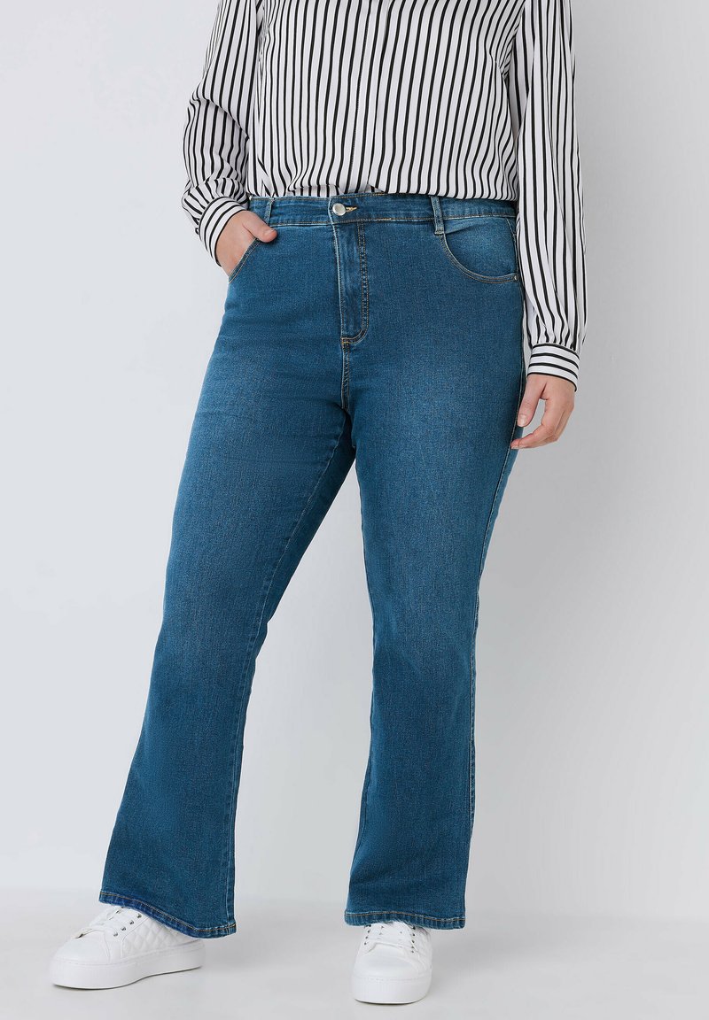 Jeans de mezclilla azul acampanados con una cintura de altura media, que cuentan con dos bolsillos frontales, un cierre de botón en la parte delantera y detalles de costura visibles.
