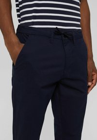 Granatowe spodnie wykonane z mieszanki bawełny, charakteryzujące się dopasowanym krojem, bocznymi kieszeniami oraz regulowanym paskiem w talii dla większego komfortu.