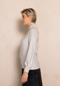 Light gray long-sleeve top with a mock turtleneck and smocked cuffs. Made from a shiny, textured fabric, featuring a slim fit.