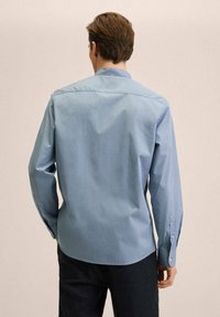 Camicia button-up azzurro chiaro con maniche lunghe, caratterizzata da un colletto classico, orlo dritto e una texture sottile. Nessun motivo o accento visibile.