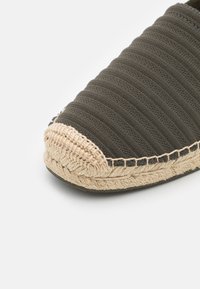 Tmavě šedé espadrilky s prošívaným textilním svrškem a špičkou z přírodního jutového lana. Vyznačují se texturovaným povrchem a plochou gumovou podrážkou.