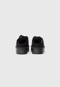 Chaussures en daim noir avec une doublure douce et duveteuse. Forme arrondie et épaisse semelle en caoutchouc noir avec une surface texturée. Pas de lacets ni de matériel visible.