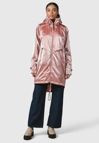 Rožinė metalinė lietpaltis su įdėtu gaubtu, priekyje užtrauktuku ir nuskabomu raišteliu. Yra didelės priekinės kišenės ir laisvas kirpimas. Dėvima su tamsiais džinsais.