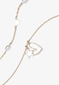 Collier doré avec un pendentif en forme de cœur incrusté de blanc et un charm étoile, agrémenté de petites perles transparentes le long de la chaîne.