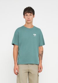 Teal cotton t-shirt with a relaxed fit, short sleeves, and a small white graphic featuring two crossed paddles on the chest.