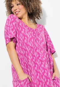 Abito rosa con maniche corte, caratterizzato da una vestibilità ampia, scollatura rotonda e un motivo astratto bianco; include tasche laterali e una texture morbida.