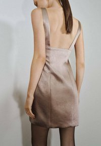 Vestido corto y ajustado en tejido metálico color rosa con una textura suave, tirantes anchos y espalda baja, combinado con medias negras transparentes.