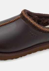 Brown leather slipper with a stitched accent and braided trim along the collar. Features soft lining and a rubber outsole for traction.
