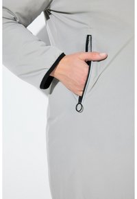 Šedá vycpaná bunda s kapsou na zip a černými akcenty. Tkanina má hladký povrch a mírně lesklý vzhled.