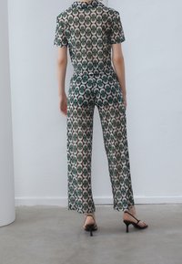 Sheer, patterned outfit with green and beige circular designs; short sleeves, wide legs, and black heels complete the look.