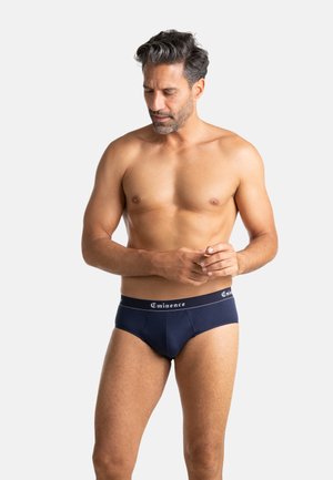 Culottes en coton bleu marine avec une ceinture élastique arborant le logo "Eminence" en blanc. Texture lisse, coupe ajustée et taille mi-haute.