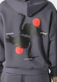 Námornícka mikina s čiernymi grafikami jeřábů a dvěma červenými kruhovými akcenty. Text "IRASUTO STUDIOS" je vyobrazen bílou barvou na zadní straně.