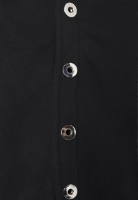 Černé oblečení s hladkou texturou, které má po celé délce stříbrné patentky. Tkanina vypadá jako elastická a přiléhavá.