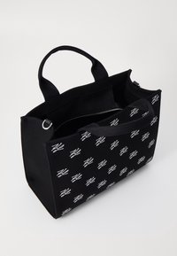 Musta suorakaiteen muotoinen kangaskassi, jossa on kaksinkertaiset kahvat, valkoinen toistuva logokuvio ja osittain avoin vetoketjullinen lokero sisällä.