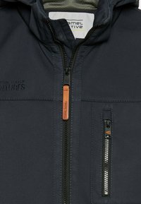 Marineblaues Kapuzenshirt aus strukturiertem Stoff, mit Frontreißverschluss und zwei Reißverschlusstaschen. Mit orangefarbenem Leder-Ziehriemen und Logo auf der Brust.