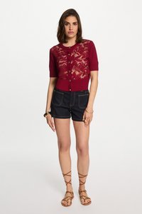 Bordeaux korte mouwen cardigan met kantpatroon en knopen, gecombineerd met donkere spijkerbroekshorts en bruine sandalen met bandjes.
