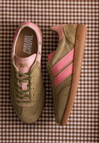 Paire de baskets de la marque Caval en daim vert olive avec bandes et accents en cuir rose, lacets verts et semelle en caoutchouc marron sur tissu à carreaux.