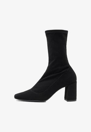 Czarne botki do kostki z spiczastym noskiem i wysokim, blokowym obcasem. Wykonane z gładkiego, elastycznego materiału z widocznymi szwami wzdłuż połączeń.