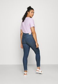 Light purple t-shirt paired with high-waisted blue denim jeans. Jeans feature two back pockets and a branded tag on the waistband.