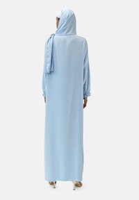 Lichtblauwe jurk met lange mouwen, losvallend model en elastische manchetten. Heeft bijpassende hijab, gladde textuur en vloeiende silhouet.