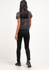 Jean en denim noir avec une coupe slim et des poches arrière, complété par un haut à manches courtes de couleur gris foncé, légèrement brillant.