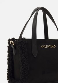 Borsa a mano in suede nero con un accento in pelliccia nera soffice e testurizzata e hardware dorato. Presenta due manici in pelle e un logo frontale.