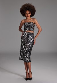 Ensemble deux pièces noir en sequins comprenant un crop top sans bretelles et une jupe longueur genoux, tous deux avec une surface brillante et réfléchissante.