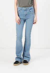 Light blue flared jeans with a high waist, five pockets, and tonal stitching. Paired with black sneakers featuring a beige sole.