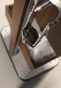 Silver stainless steel watch with a mesh strap, featuring a round case and a dark engraved back displaying the brand name and water resistance.