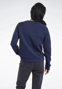 Mörkblå sweatshirt med rund hals, raglanärmar och ribbad nederkant. Kombinerad med mörkgrå jeans, vilket framhäver en avslappnad stil.