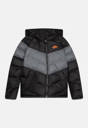 Chaqueta tipo puffer negra y gris con capucha, con un diseño en forma de chevron, cierre frontal, dos bolsillos laterales y un logo de Nike en color naranja en el pecho.