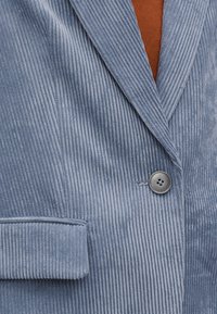 Lichtblauwe corduroy blazer met verticale ribbels, ingesneden revers en een enkele grijze knoop. Voorzien van een zakopzetstuk op de mouw.