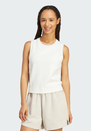 Haut de sport sans manches blanc avec un col rond, présentant une texture subtile et un petit logo. Associé à un short beige, également avec un détail de logo.