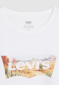 Witte katoenen T-shirt met een kleurrijk berg- en woestijnlandschap onder het "Levi's" logo in grote, vetgedrukte letters. Etiket zichtbaar in de halslijn.