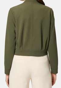 Olivgrüne, kurz geschnittene Jacke mit Stehkragen, geripptem Bund und langen Ärmeln. Glatte Textur mit sichtbaren Nähdetails auf der Rückseite.