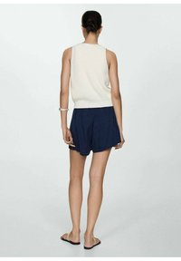 Top de tirantes sin mangas de punto blanco y pantalones cortos azul marino con cintura elástica. Textura suave, ajuste informal y sandalias completan el conjunto.