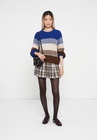 Strickpullover mit blau, beige und braunen Streifen, kombiniert mit einem karierten Minirock. Accessoires umfassen eine kleine schwarze Tasche und dunkle Strumpfhosen.