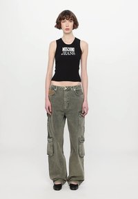 Melna bezpiedurkņu blūze ar baltu "MOSCHINO JEANS" logotipu, ko papildina brīvi pieguļošas olīvu zaļas kravas bikses ar vairākām kabatām.