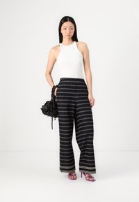 Λευκή αμάνικη μπλούζα συνδυασμένη με μαύρο παντελόνι σε φαρδιά γραμμή με διακοσμητικά μοτίβα διαμαντιών. Τα αξεσουάρ περιλαμβάνουν μια μαύρη τσάντα και μωβ σανδάλια με τακούνι.