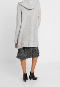 Light grey knitted cardigan with a hood, textured pattern, and ribbed hem, worn over a black leopard print dress and ankle boots.