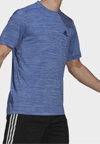 Sininen lyhythihaisen urheilupaita, jossa on teksturoitu raidallinen kuvio ja musta Adidas-logo vasemmassa rinnassa. Istuu tiukasti vartalonmyötäisesti.