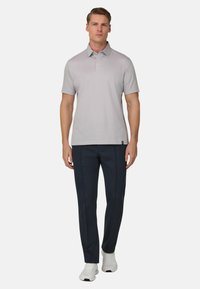 Hellgraues Poloshirt mit Kragen, kombiniert mit dunkelblauen Hosen. Das Modell trägt weiße Sportschuhe und steht aufrecht.