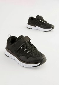Baskets de sport noires avec tige en maille, semelle en caoutchouc, sangle réglable et lacets élastiques. Présente des accents blancs et des détails texturés.