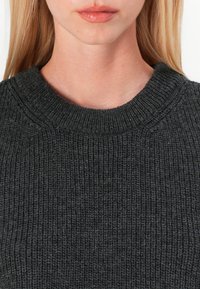 Pull en maille gris à col rond. La texture semble épaisse avec un tissu doux en tricot et de subtiles variations dans le fil.