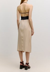 Beige midi-rok met een getextureerd patroon, aansluitende zwarte torso, dunne bandjes en een rits aan de achterkant. Gecombineerd met zwarte sandalen met blokhakken en bandjes.