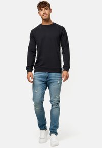 Sort sweatshirt med lange ærmer og rund hals, kombineret med lyseblå slidte jeans og hvide sneakers.