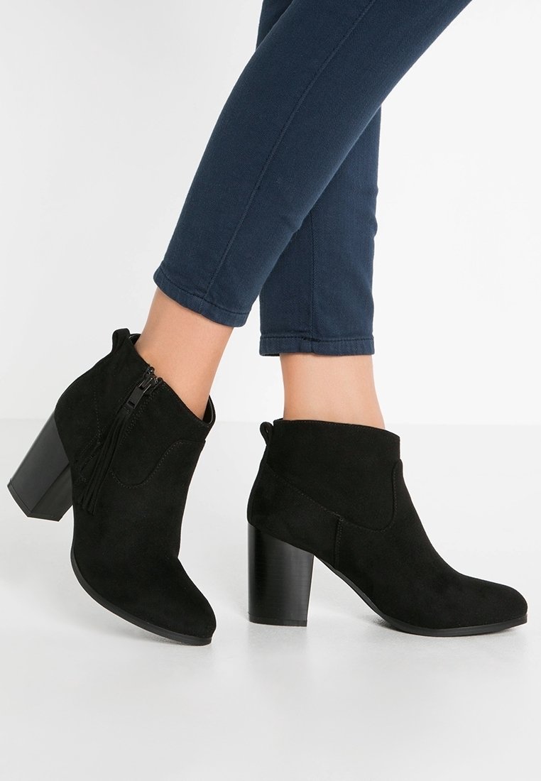 Mustat mokkanahkaiset nilkkurit, joissa on paksu korko, franssit yksityiskohtina ja sivuvetoketju, yhdistetty dark blue -värisiin lyhyisiin housuihin.