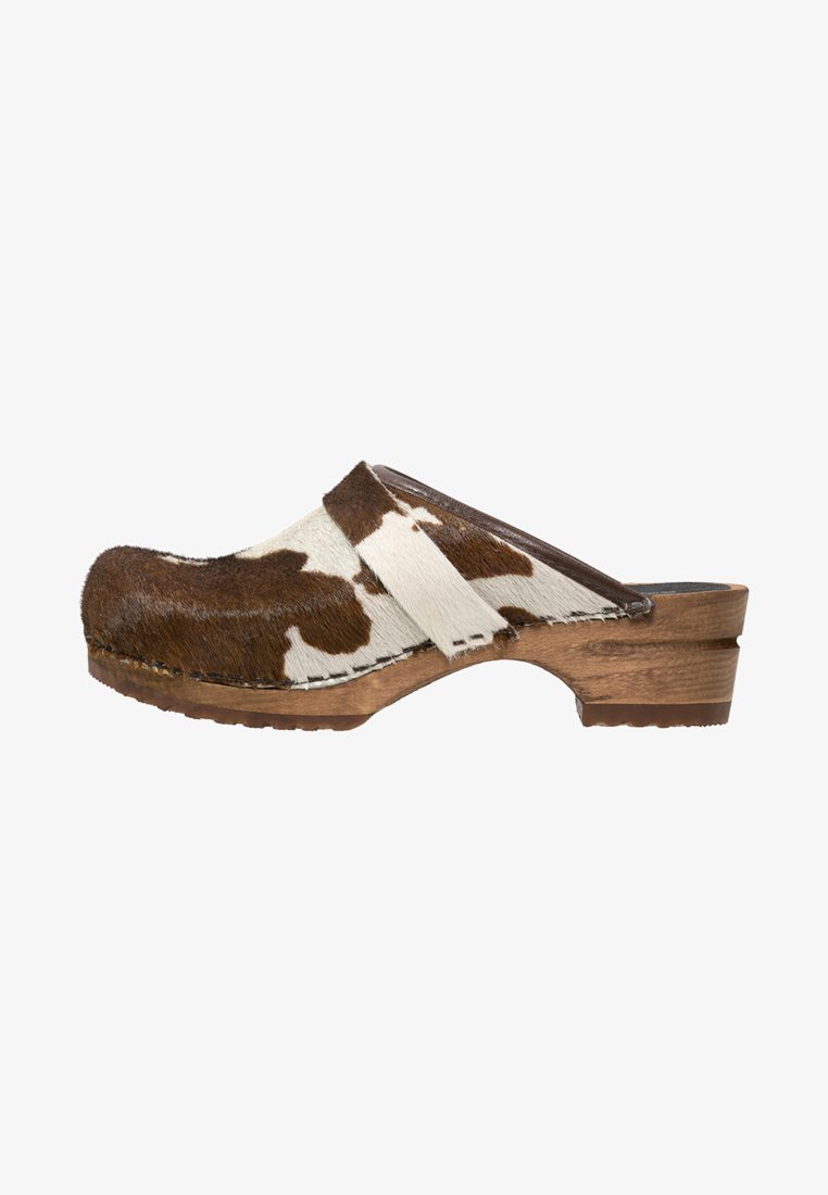 Brown and white cow-print clogs with a wooden base. Features a smooth leather strap and textured fur-like upper. Side view.